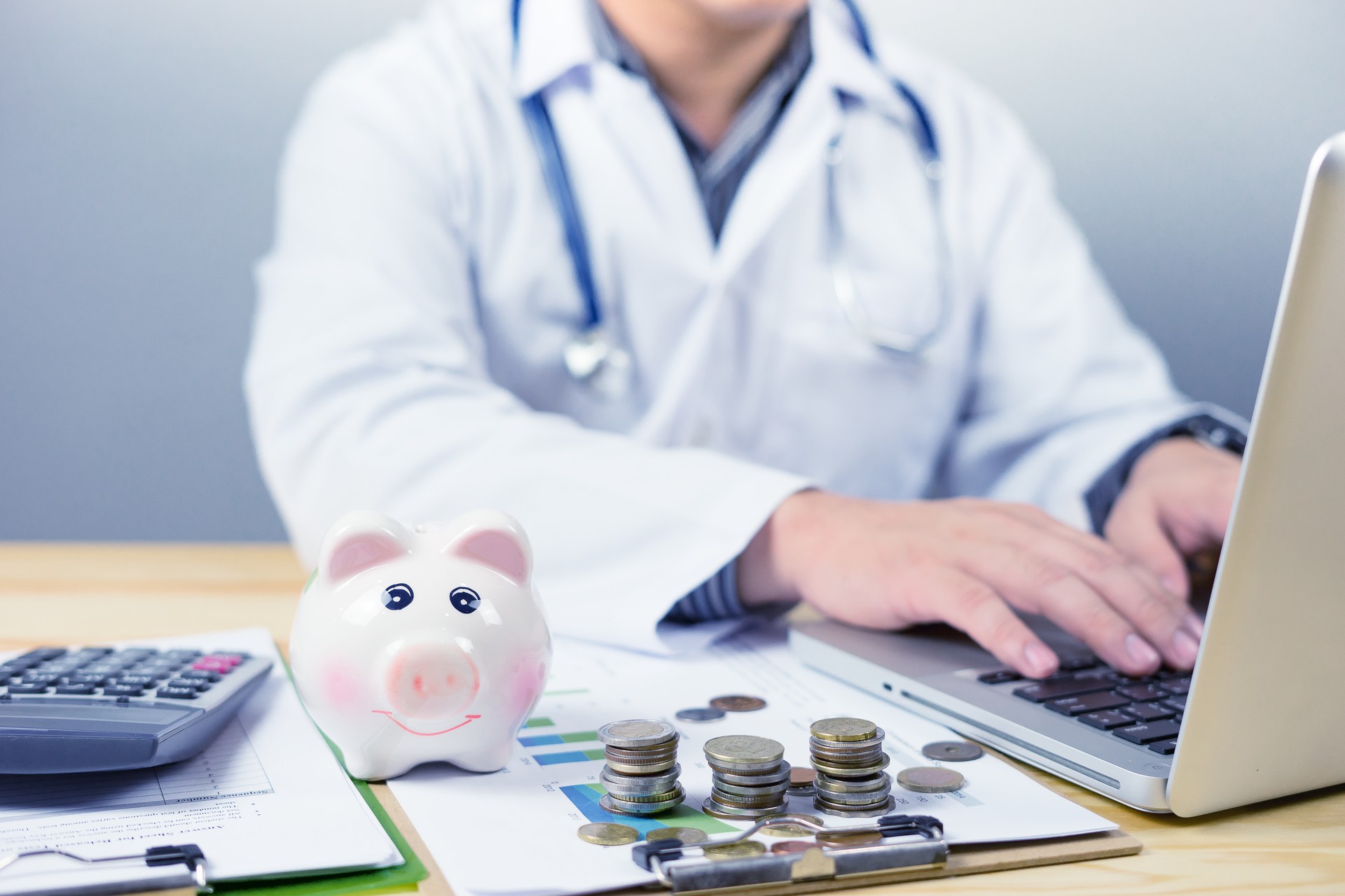 young medical doctor caucasian healthcare professional wearing a white coat with stethoscope in hospital,calculates on an electronic calculator laptop,medical fee concept,selective focus,vintage color