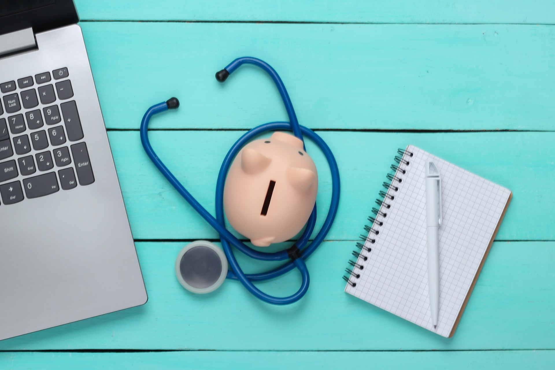 Laptop with piggy bank, stethoscope, notebook on a blue background. Online doctor. Top view. Flat lay