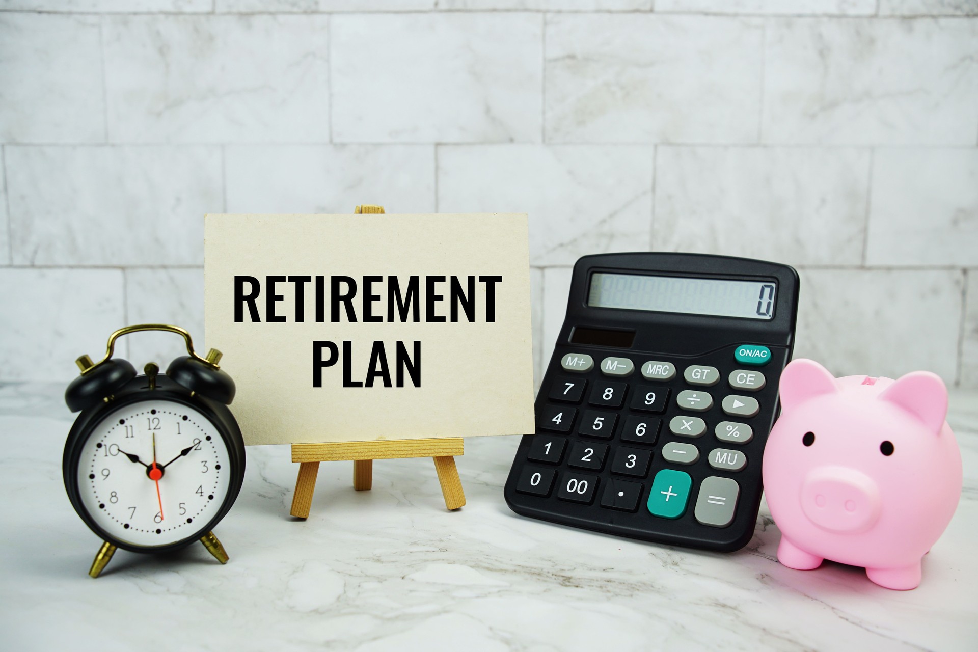 Retirement Plan text written on paper card with piggy saving, calculator and alarm clock on marble background