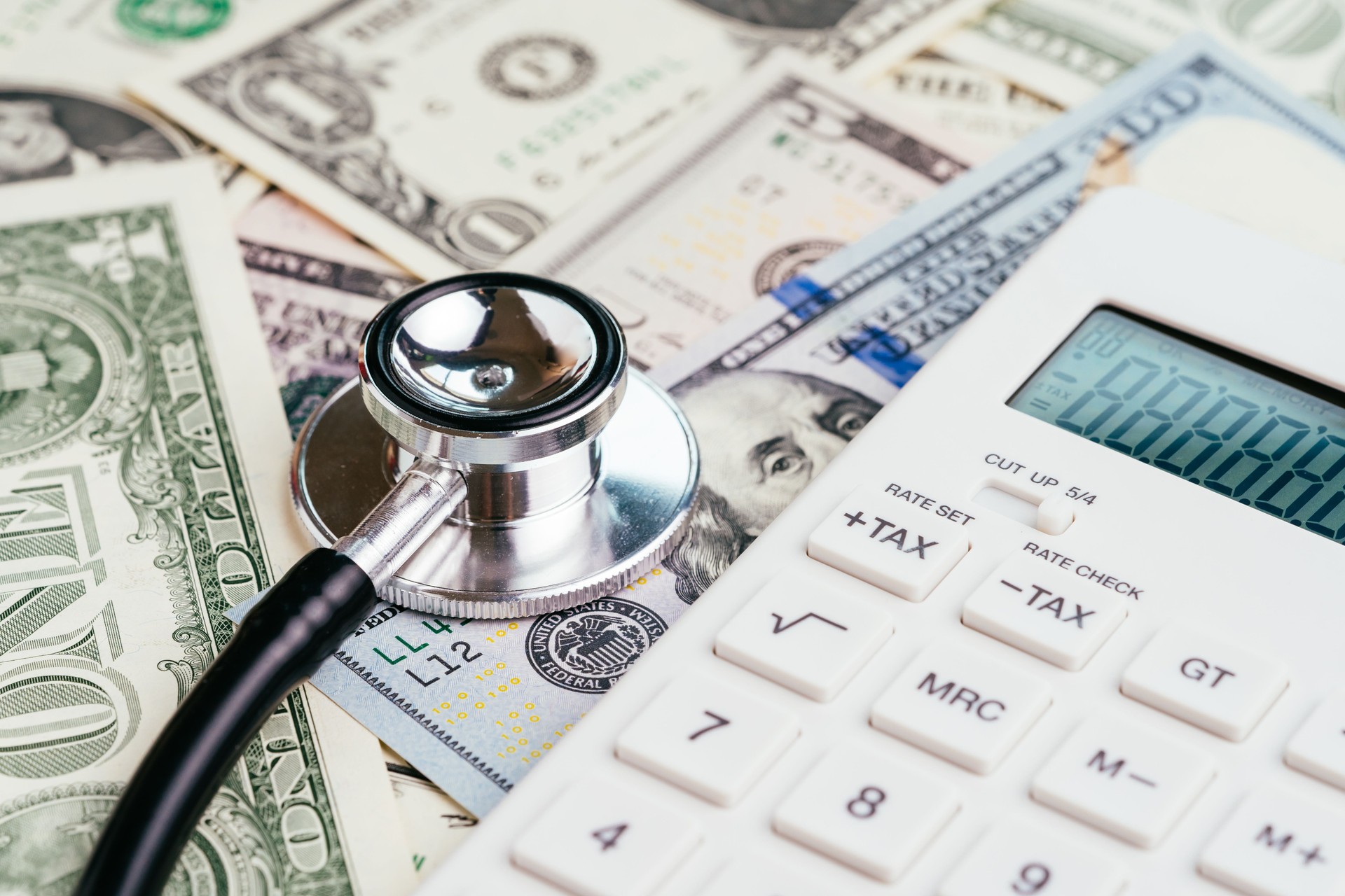 Financial health check, tax or medical and health care expense concept, stethoscope put on FED federal reserve emblem on US dollar banknotes with white calculator, debt and revenue ratio