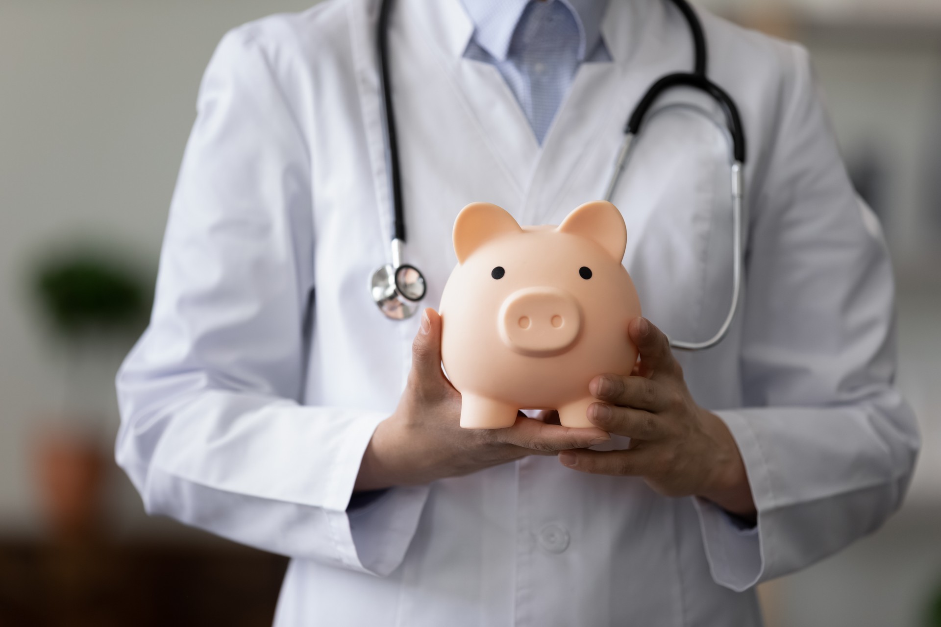 Crop close up female doctor physician holding pink piggy bank
