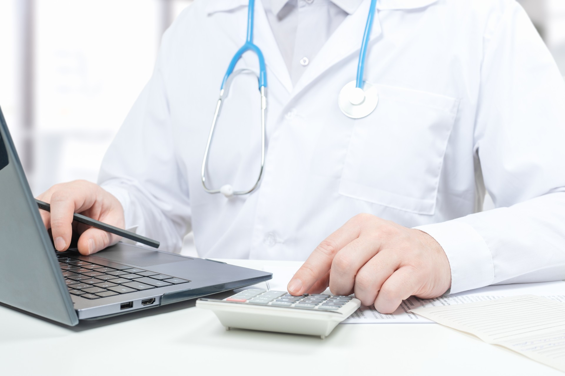 Doctor working with medical statistics and financial reports. doctor counts on calculator and enters data into laptop. male doctor using laptop and calculator at office